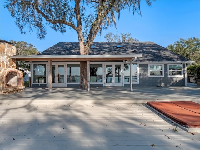 rear view of house with french doors, a wooden deck, and an outdoor stone fireplace