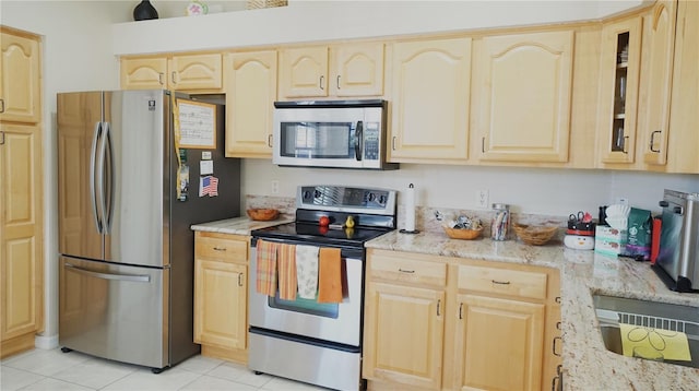 kitchen with light tile patterned floors, light brown cabinets, stainless steel appliances, and light stone counters