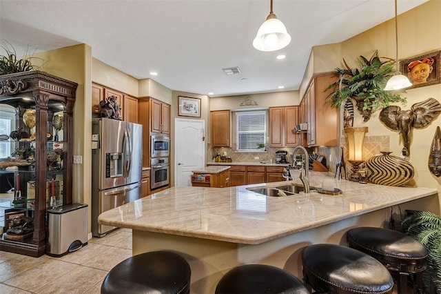 kitchen with kitchen peninsula, appliances with stainless steel finishes, light stone counters, sink, and decorative light fixtures