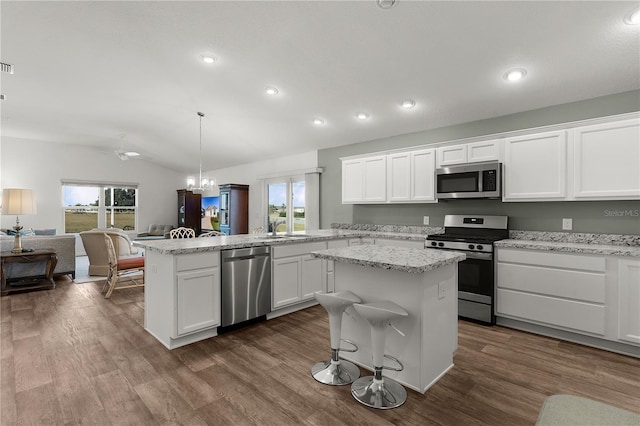 kitchen with pendant lighting, a center island, white cabinetry, stainless steel appliances, and vaulted ceiling