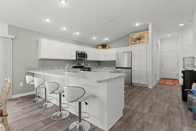 kitchen with a breakfast bar area, stainless steel appliances, lofted ceiling, and white cabinetry