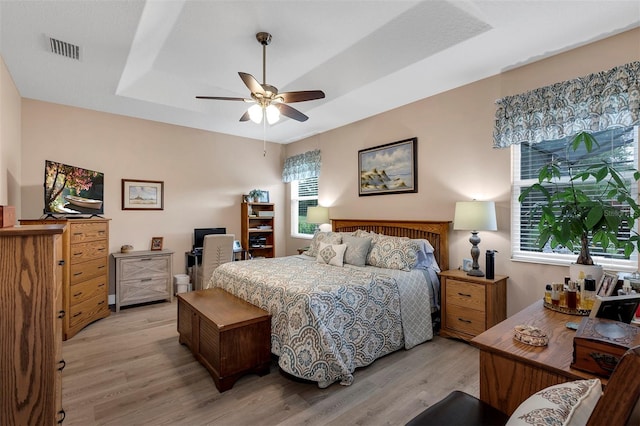 bedroom featuring light hardwood / wood-style floors, a raised ceiling, and ceiling fan