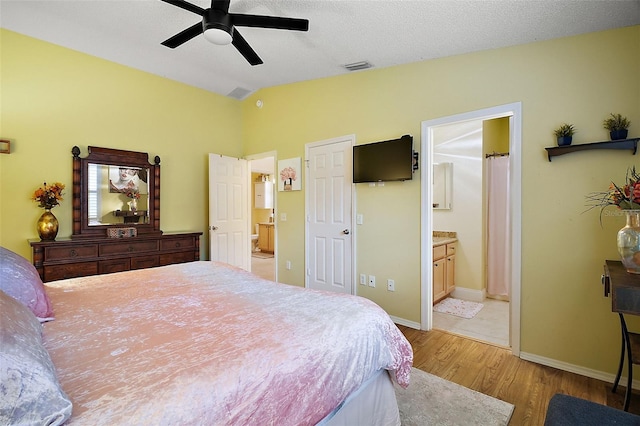 bedroom with ensuite bathroom, ceiling fan, lofted ceiling, light wood-type flooring, and a textured ceiling