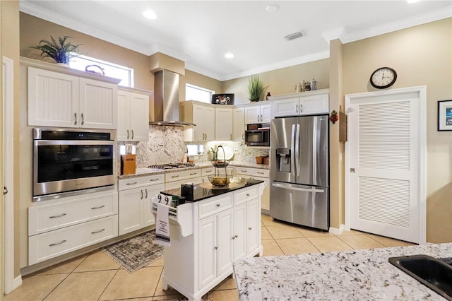 kitchen featuring backsplash, wall chimney exhaust hood, stainless steel appliances, crown molding, and white cabinetry