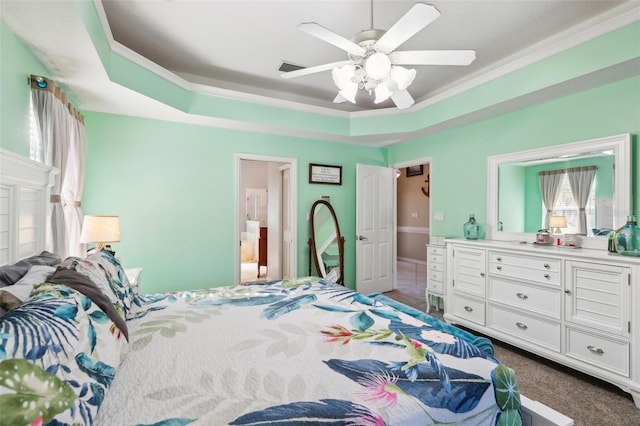 carpeted bedroom featuring ceiling fan, ornamental molding, ensuite bathroom, and a tray ceiling