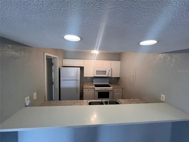 kitchen featuring a textured ceiling, white cabinets, kitchen peninsula, and white appliances