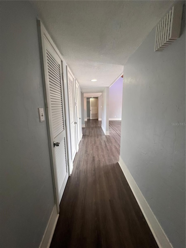 hallway with a textured ceiling and dark hardwood / wood-style floors