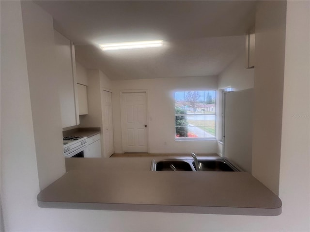 kitchen with sink, white cabinetry, gas range gas stove, and kitchen peninsula