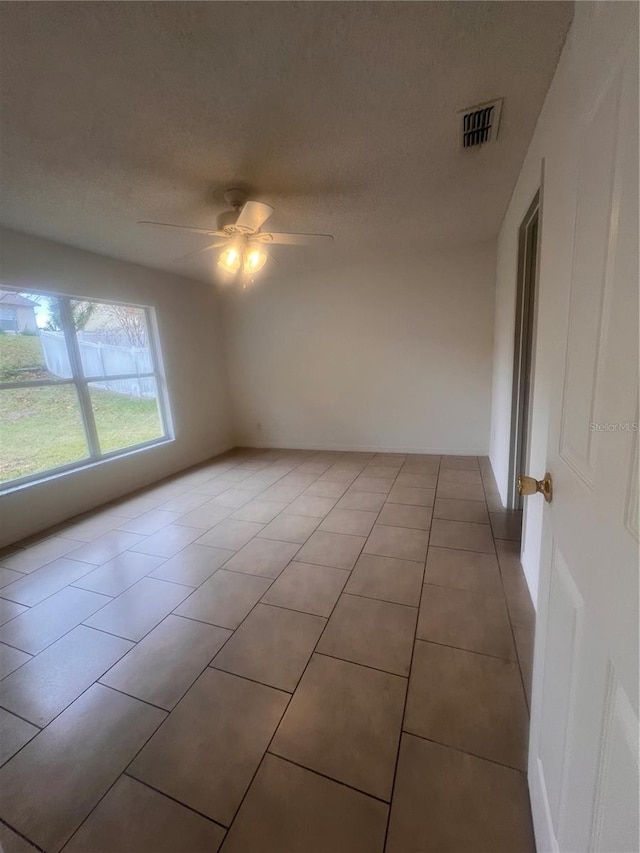 empty room featuring a textured ceiling, ceiling fan, and light tile patterned floors