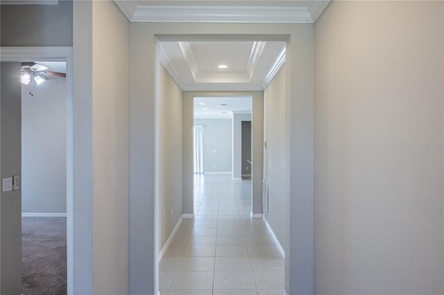 corridor featuring light tile patterned floors, a raised ceiling, and crown molding