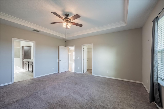 unfurnished bedroom featuring connected bathroom, ceiling fan, a raised ceiling, crown molding, and light colored carpet