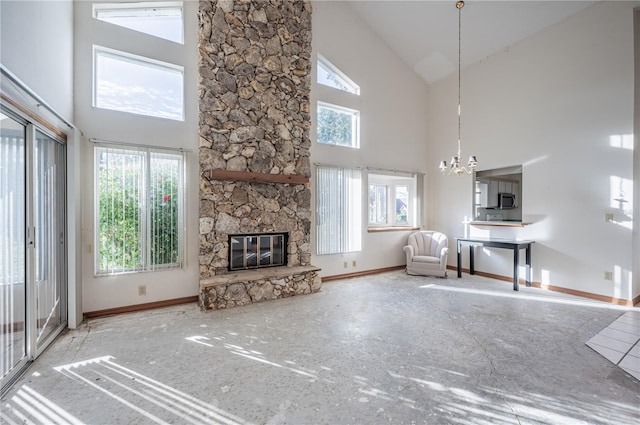 unfurnished living room with a stone fireplace, high vaulted ceiling, and a notable chandelier