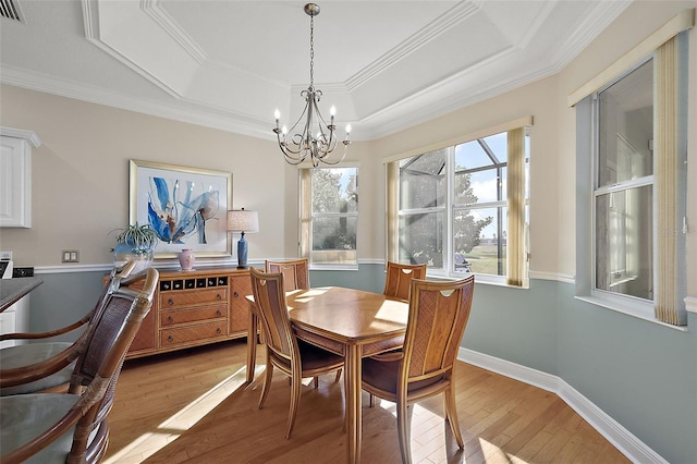 dining area with a tray ceiling, crown molding, a chandelier, and light wood-type flooring