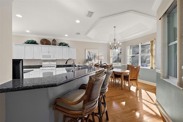 kitchen featuring a chandelier, white appliances, a tray ceiling, white cabinets, and light wood-type flooring