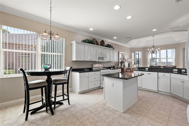 kitchen featuring white cabinets, white appliances, a tray ceiling, pendant lighting, and a chandelier