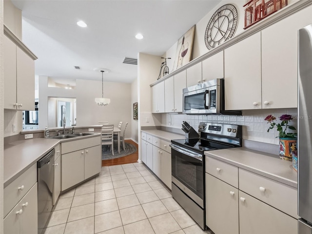 kitchen with stainless steel appliances, sink, white cabinets, and decorative light fixtures