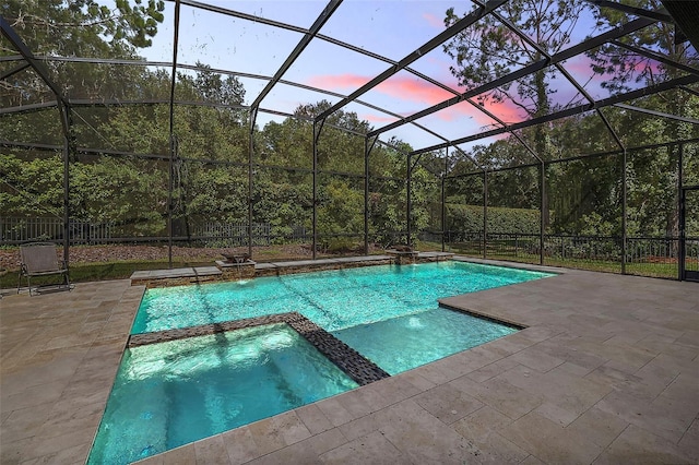 pool at dusk with a lanai, a patio area, an in ground hot tub, and pool water feature