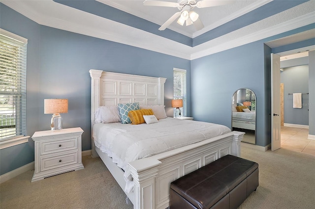 carpeted bedroom with a tray ceiling, connected bathroom, ceiling fan, and crown molding