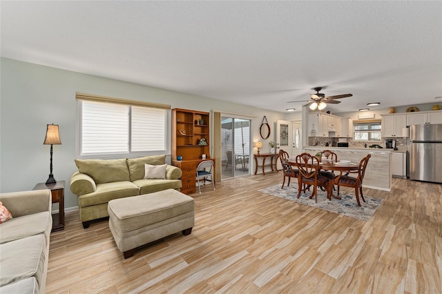 living room featuring ceiling fan, a textured ceiling, and light wood-type flooring