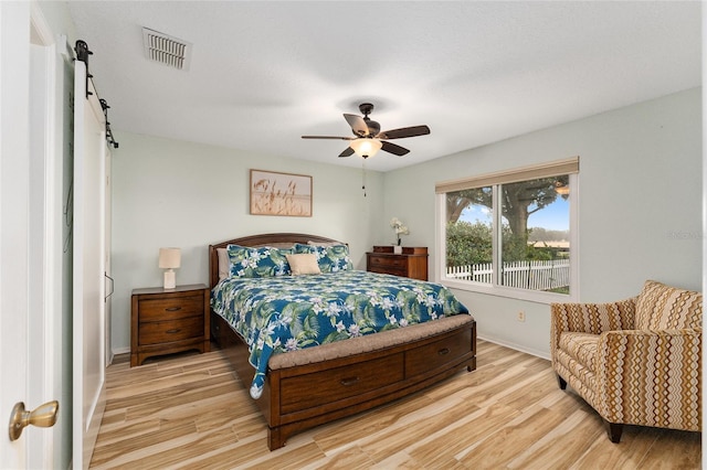 bedroom with ceiling fan, a barn door, and light wood-type flooring