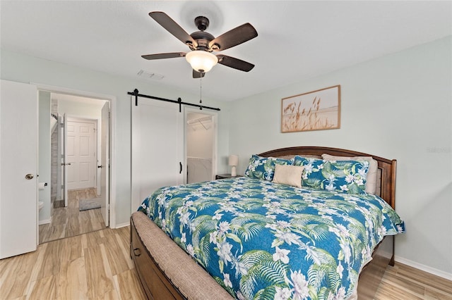 bedroom featuring a barn door, ceiling fan, and light wood-type flooring