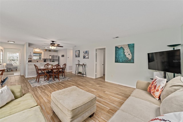 living room featuring ceiling fan, a textured ceiling, and light wood-type flooring