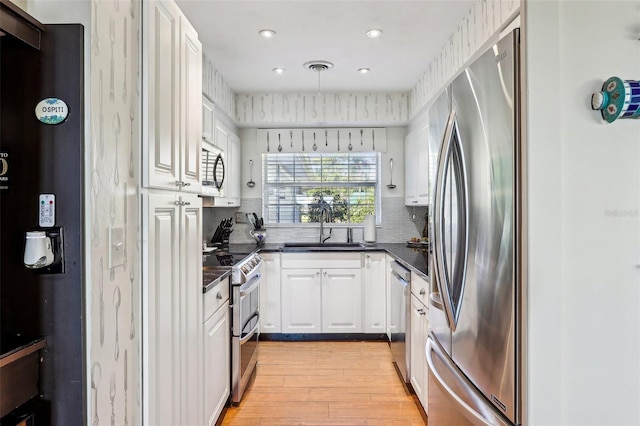 kitchen featuring appliances with stainless steel finishes, light wood-type flooring, tasteful backsplash, sink, and white cabinetry