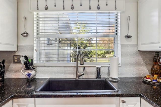 kitchen featuring backsplash, dark stone countertops, white cabinetry, and sink