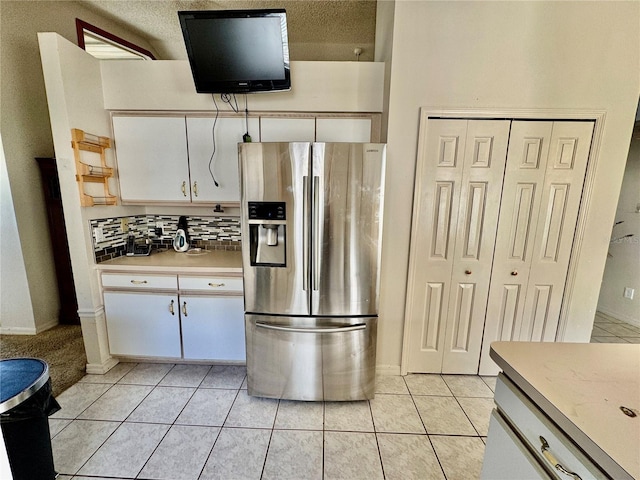 kitchen featuring light tile patterned floors, stainless steel fridge, a textured ceiling, decorative backsplash, and white cabinets