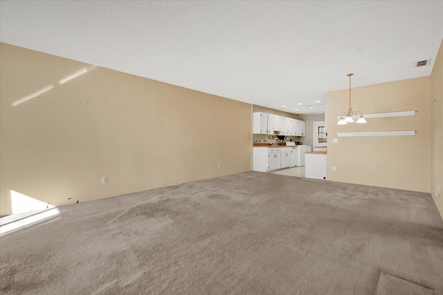 unfurnished living room with light colored carpet, a chandelier, and a textured ceiling