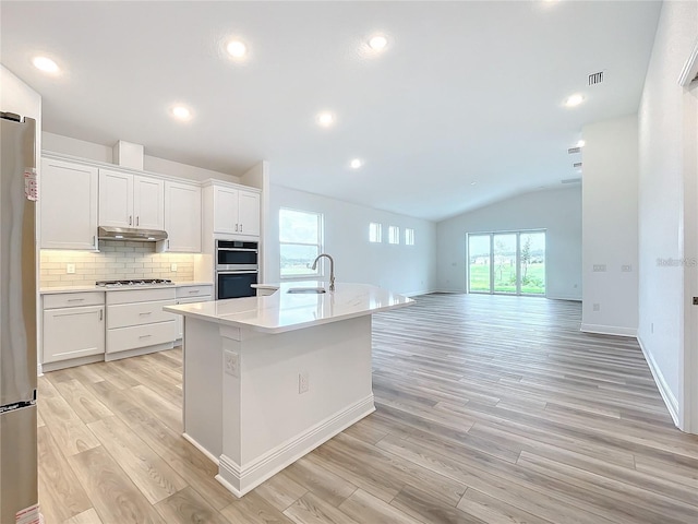 kitchen featuring lofted ceiling, backsplash, a kitchen island with sink, white cabinetry, and stainless steel appliances