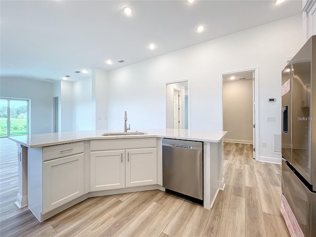 kitchen with sink, white cabinets, stainless steel appliances, and a center island with sink