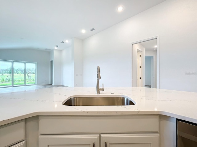 kitchen with wine cooler, light stone counters, sink, and vaulted ceiling