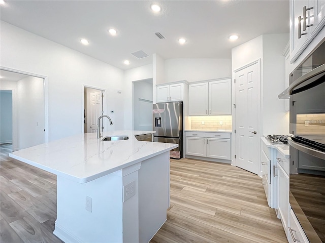 kitchen with sink, decorative backsplash, a center island with sink, white cabinets, and appliances with stainless steel finishes