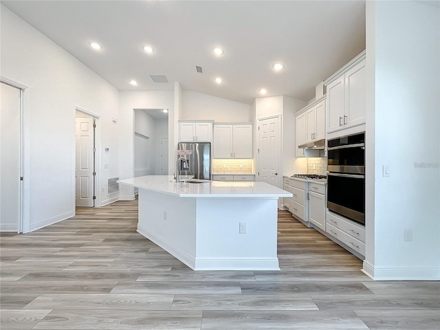 kitchen featuring white cabinets, decorative backsplash, a kitchen island with sink, and appliances with stainless steel finishes