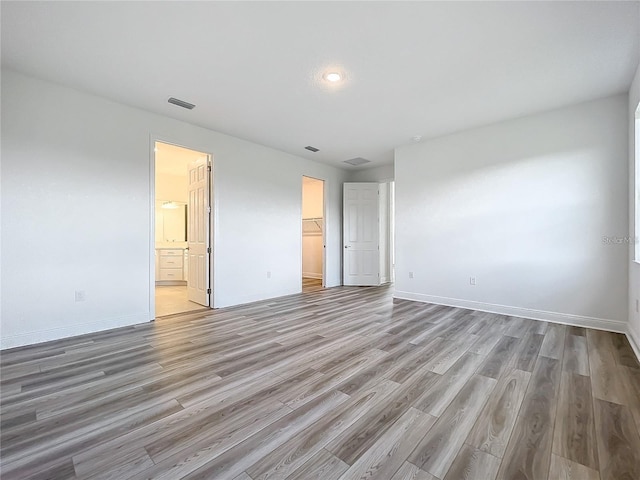 unfurnished bedroom featuring light wood-type flooring, a walk in closet, ensuite bath, and a closet