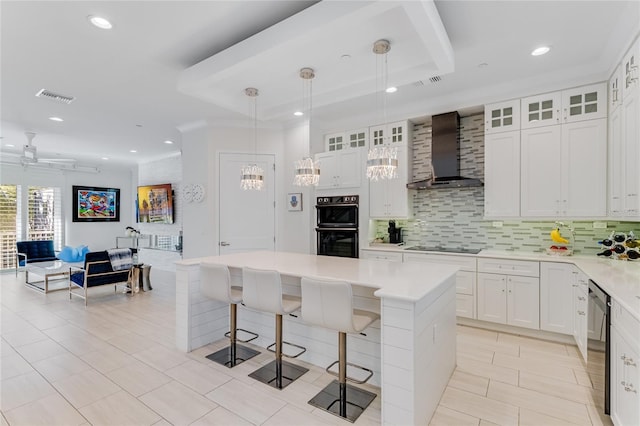 kitchen with pendant lighting, white cabinets, a kitchen island, and wall chimney range hood