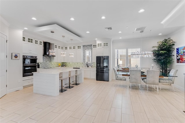 kitchen with a large island, wall chimney range hood, white cabinets, and black appliances