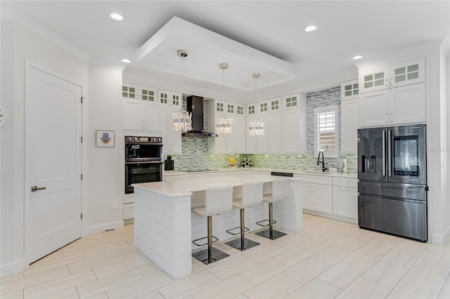 kitchen with black appliances, a center island, hanging light fixtures, wall chimney range hood, and white cabinets