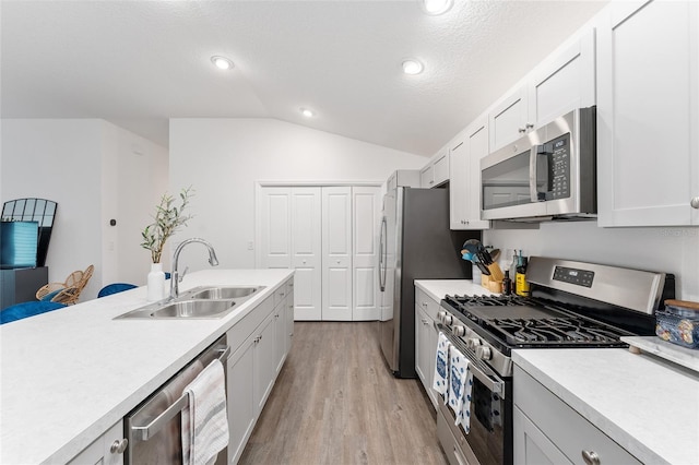 kitchen with white cabinetry, vaulted ceiling, appliances with stainless steel finishes, sink, and light hardwood / wood-style flooring