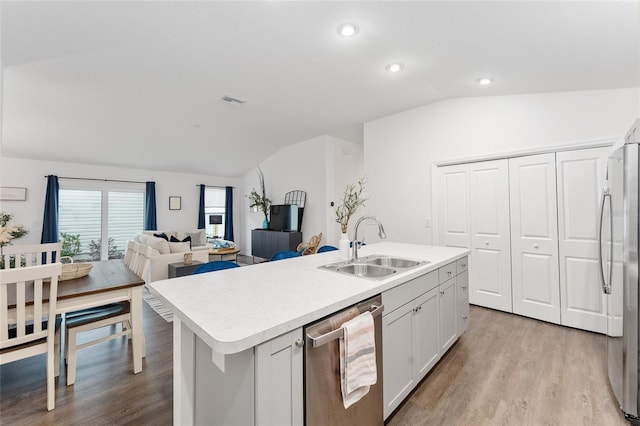 kitchen with lofted ceiling, stainless steel appliances, a center island with sink, and sink