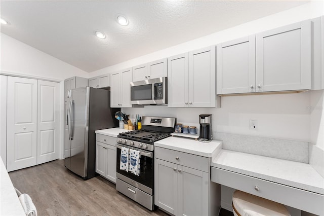 kitchen with lofted ceiling, stainless steel appliances, light wood-type flooring, and a textured ceiling