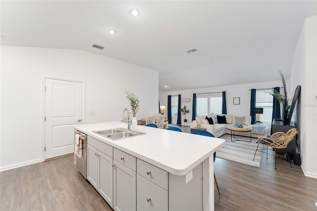 kitchen featuring dishwasher, vaulted ceiling, an island with sink, sink, and light hardwood / wood-style flooring