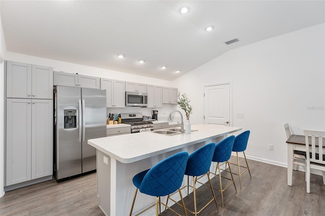 kitchen with a center island with sink, a kitchen bar, lofted ceiling, appliances with stainless steel finishes, and sink