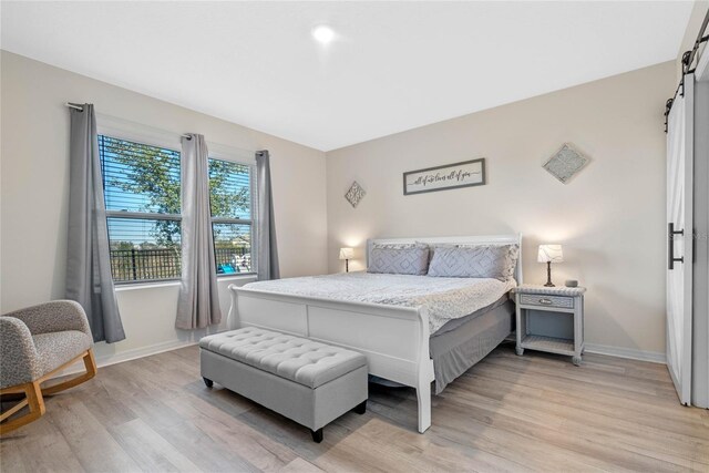 bedroom featuring a barn door and light hardwood / wood-style flooring