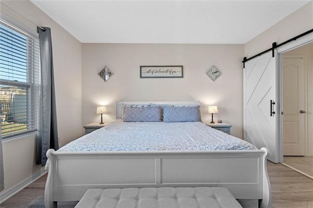 bedroom featuring a barn door, multiple windows, and light wood-type flooring