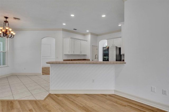 11941 Graces Way, Clermont, FL 34711 - kitchen featuring freestanding refrigerator, arched walkways, white cabinets, crown molding, and a peninsula