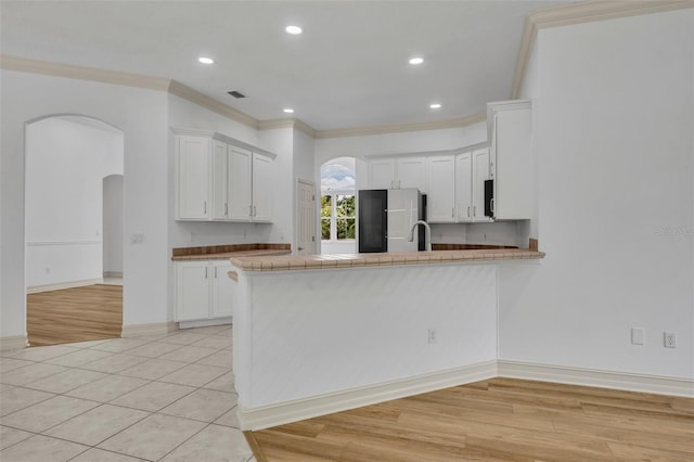 11941 Graces Way, Clermont, FL 34711 - kitchen with fridge, arched walkways, a peninsula, ornamental molding, and white cabinetry