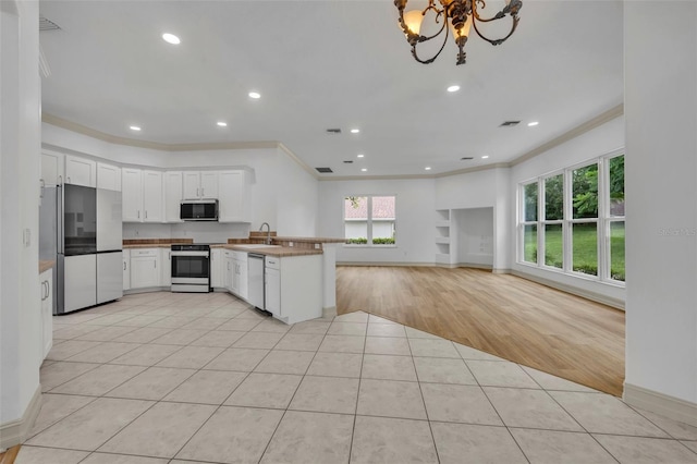11941 Graces Way, Clermont, FL 34711 - kitchen with appliances with stainless steel finishes, crown molding, a peninsula, light tile patterned flooring, and white cabinetry