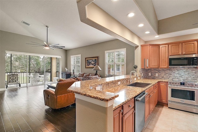 kitchen featuring kitchen peninsula, light stone countertops, stainless steel appliances, ceiling fan, and sink